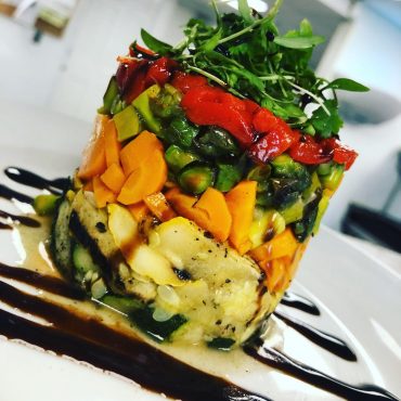 roasted vegetable napoleon stacked four layers high with herb oil drizzle on a white plate