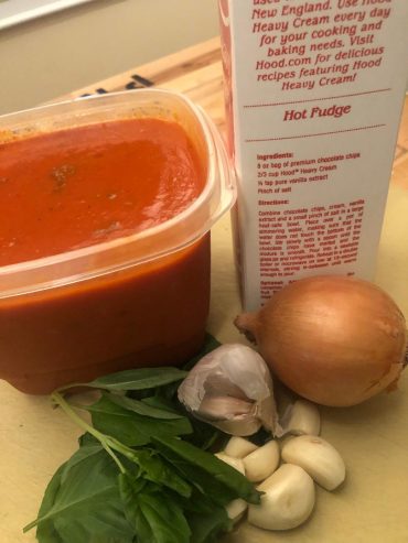tomato bisque soup in a white bowl with cream swirl fresh basil and crostini