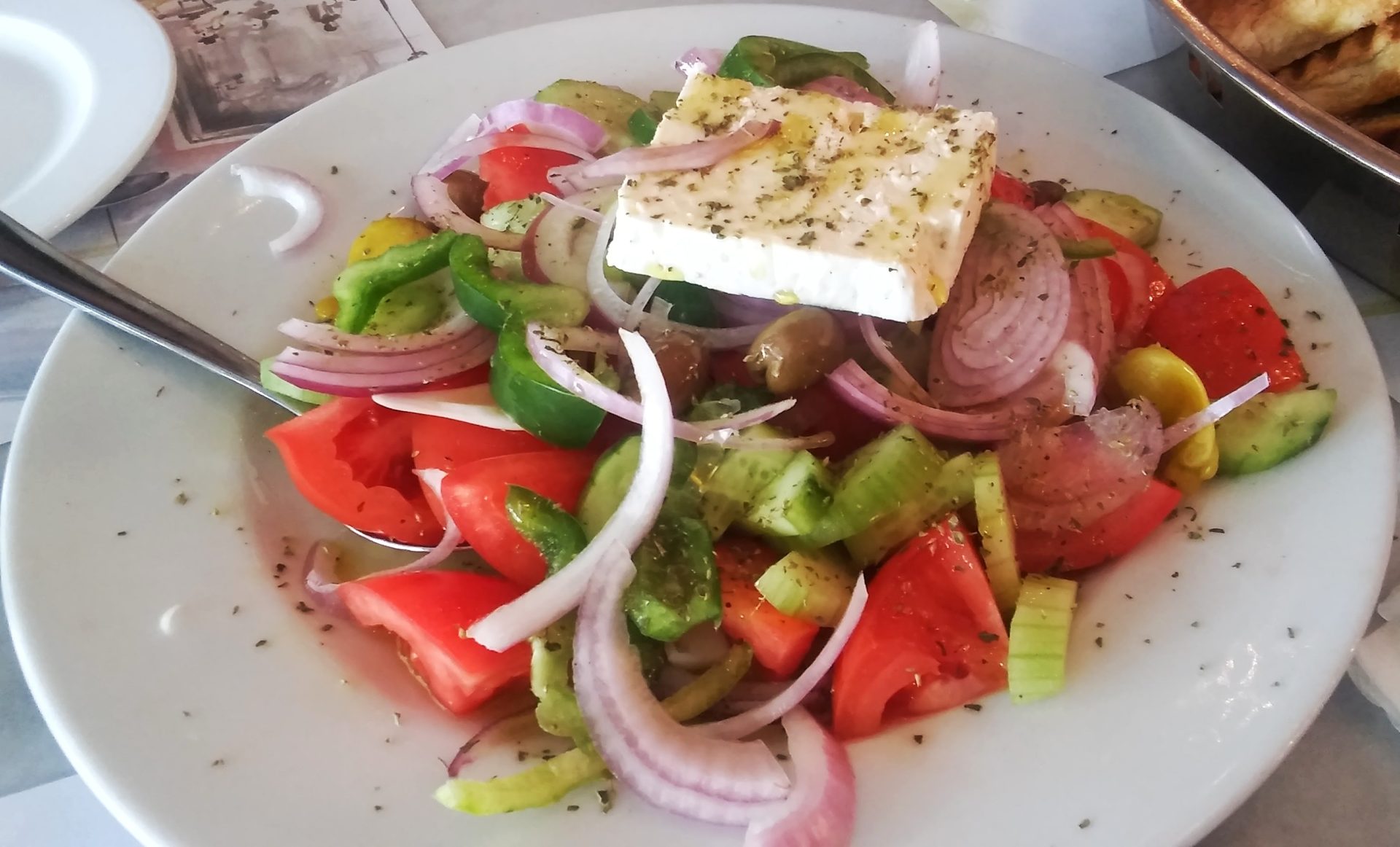 Traditional Greek horiatiki village salad with ripe tomatoes, cucumber, Kalamata olives and a thick slab of feta cheese drizzled with olive oil