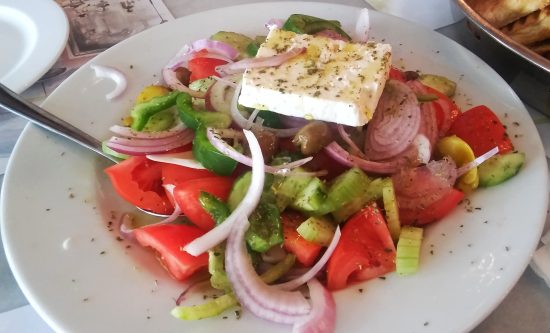 Traditional Greek horiatiki village salad with ripe tomatoes, cucumber, Kalamata olives and a thick slab of feta cheese drizzled with olive oil