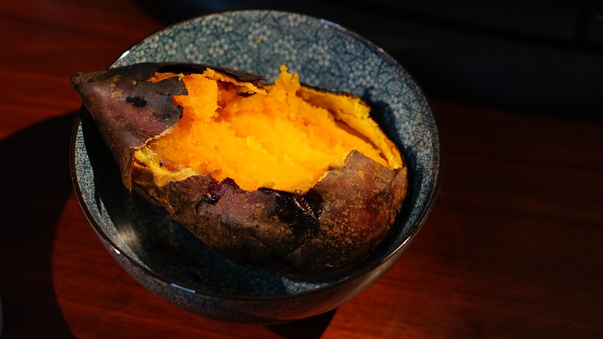 Roasted sweet potato split open showing vibrant orange caramelized flesh in a ceramic bowl on a wooden surface
